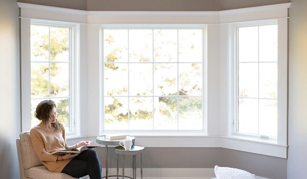 Woman reading by white bay windows with grilles